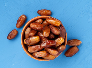 Dates, dried fruits in bowl. Traditional food of middle East, North Africa. Top view, bright blue wooden background.