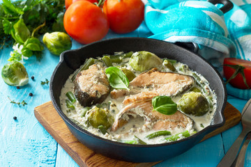 Red fish and vegetables baked (brussels sprouts, green beans) in cream sauce in a frying pan in a...
