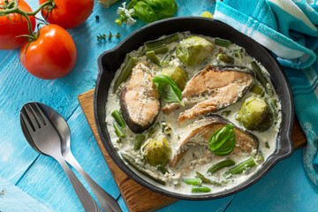 Red fish and vegetables baked (brussels sprouts, green beans) in cream sauce in a frying pan in a rustic style.