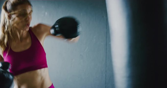 Beautiful athletic woman kickboxing, training with punching bag in the gym