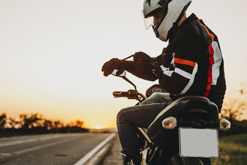 Side view of a caucasian man sitting on the motorcycle and putting his gloves preparing to start...