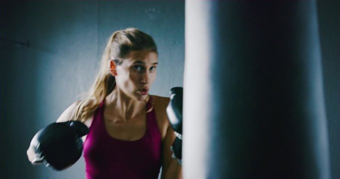 Beautiful athletic woman kickboxing, training with punching bag in the gym, slow motion