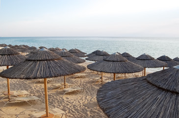 Straw umbrellas and chaise lounges on the beach in Greece.