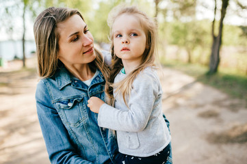 Happy smiling mother hugging her lovely little daughter outdoor. Lifestyle family. Adult cheerful female parent playing with her beautiful emotional child at nature in summer. Positive people faces.