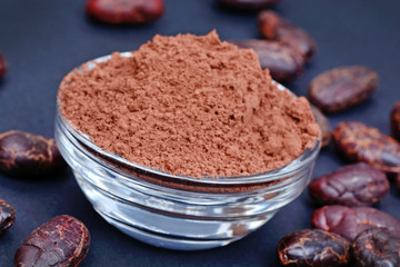 Cacao powder in a transparent bowl with beans on blue background