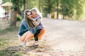 Happy smiling mother hugging her lovely little daughter outdoor. Lifestyle family. Adult cheerful female parent playing with her beautiful emotional child at nature in summer. Positive people faces.