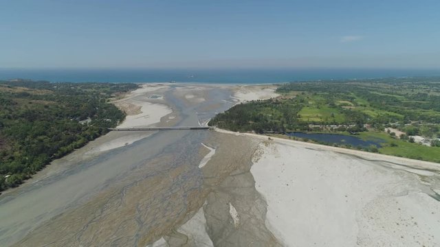 Mountain river Bucao flowing into the sea in Philippines,Luzon. Aerial view river among farmer fields flowing into the blue ocean.