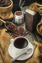 Coffee cup, coffee beans with bag, scoop  and coffee maker pot.