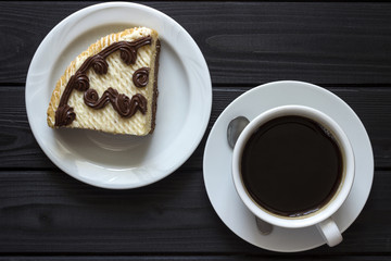 a piece of cake in a plate with a cup of coffee, on a black background, the view from the top