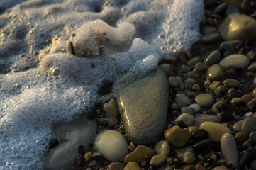 pebble stones on the sea beach, the rolling waves of the sea with foam