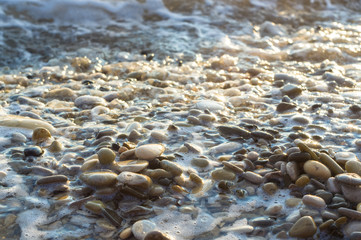 pebble stones on the sea beach, the rolling waves of the sea with foam
