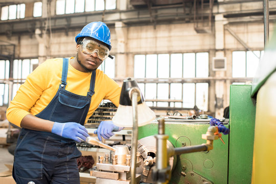Portrait shot of handsome young lathe operator wearing protective helmet and safety goggles standing at spacious production department of modern plant and looking at camera