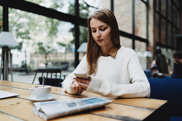 Young business woman arranging business meeting in a modern coworking space by using mobile phone application. Young freelancer female reading emails and other messages on a smartphone.