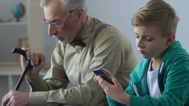Unhappy grandpa looking at grandson scrolling smartphone, lack of communication