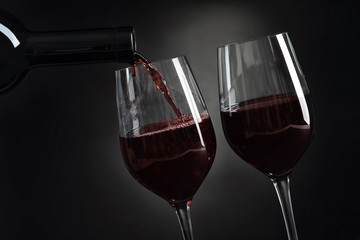 Pouring delicious red wine into glass on dark background