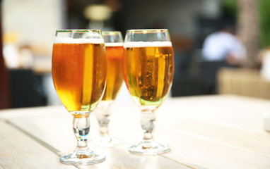 Glasses with cold beer on table against blurred background