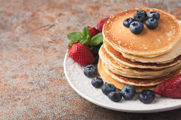 Close-up delicious pancakes, with fresh blueberries, strawberries and maple syrup on a rusty background. With copy space