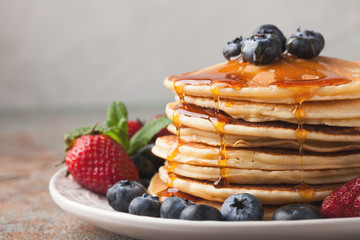 Close-up delicious pancakes, with fresh blueberries, strawberries and maple syrup on a light...