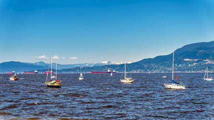 Fototapeta na wymiar Large ocean ocean going vessels and recreational boats in busy English Bay at Vancouver British Columbia, Canada with the Coast Mountain in the background