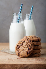 A stack of cookies with milk chocolate and two bottles of milk on a wooden table