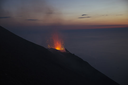 Young man watching a Stromboli volcano eruption at sunset