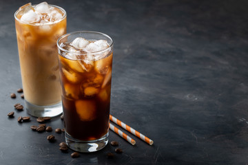Ice coffee in a tall glass with cream poured over, brown sugar and coffee beans. Cold summer drink on a dark background. With copy space