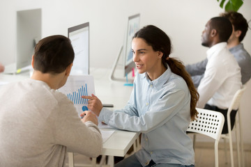 Obraz premium Smiling female worker showing financial graph to male client or colleague, explaining company statistics, talking about sales growth, sharing ideas of business successful strategy. Cooperation concept