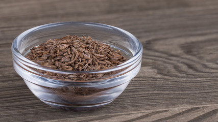 Caraway seeds in a glass bowl on a wood background. Carum carvi. Beautiful close-up of the pile of brown aromatic cumin spice with a distinctive flavor and scent.