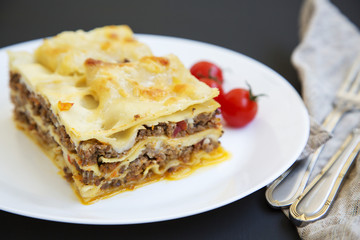 Traditional beef lasagne on a white round plate on black background, side view.