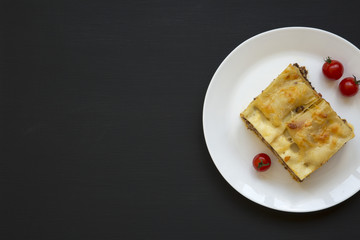 Traditional italian beef lasagne on a white round plate on black background, top view. Flat lay. Copy space.