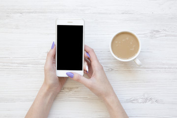 Female hands using smartphone and drinking latte, top view. Flat lay.