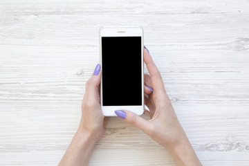 Female hands using smartphone on white wooden background, top view. Flat lay.