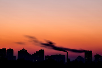 Cityscape with dramatic sky  sunset. Silhouette of buildings and smoking pipes. Urban industrial city.  Environmental pollution
