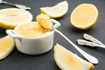Lemon curd in white jar with spoon with curd and lemon slices