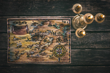 Pirate treasure map and burning candle on aged wooden table background. Treasure hunt concept. Sea travel.
