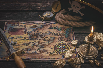 Pirate treasure map, gold nuggets, dagger and pirate hat on aged wooden table background. Sea travel.