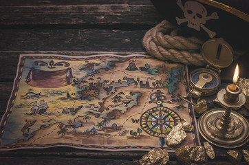 Pirate treasure map, gold nuggets and pirate hat on aged wooden table background. Sea travel.