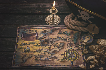 Naklejka premium Piracka skarb mapa, złociste bryłki i pirata kapelusz na starzejącym się drewnianym stołowym tle. Podróże morskie.