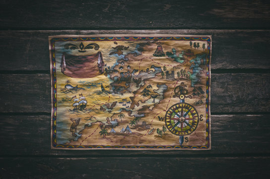 Pirate treasure map with gold mark on aged wooden table background. Top view photo.