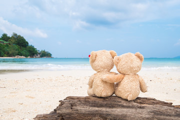 Two teddy bears sitting on the timber with sea view. Love and relationship concept. Beautiful white sandy beach in the summer. © suthisak