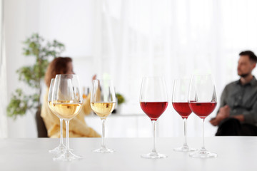 Glasses with delicious wine and blurred couple on background