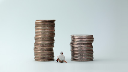 A miniature man sitting between two piles of coins.