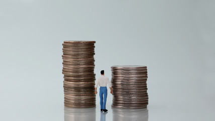 The back of a miniature man watching two pile of coins.