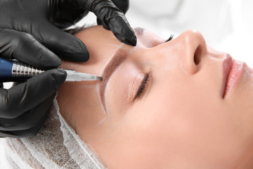 Young woman undergoing eyebrow correction procedure in salon