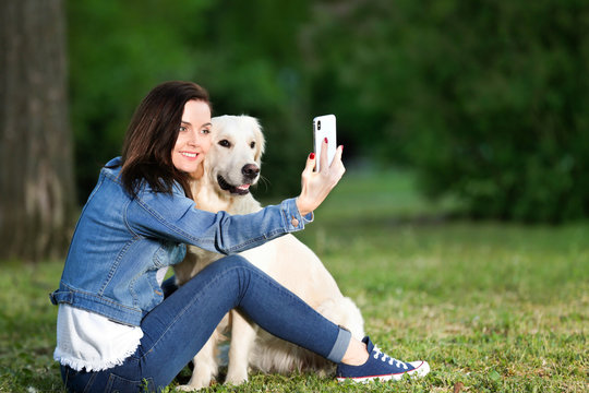 Young woman taking selfie together with her dog in park. Pet care