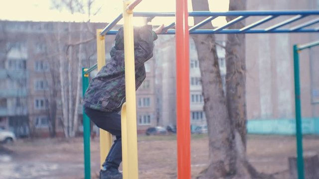 Boy crawling on the monkey bars in the yard of a city house. Games and walks on the Playground.