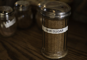 Raw brown sugar in glass sugar bowl with nametag on wooden table.