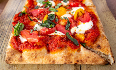 Classic Margherita Flatbread: Tomato Base, Fresh Mozzarella, Sliced Tomatoes, Basil on old rustic wood board, close up.
