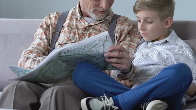 Retired man showing his travel places to grandson on map, planning trip together