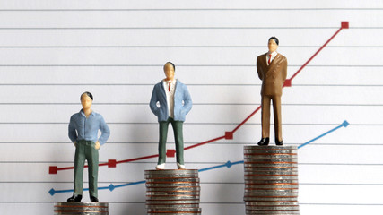 Miniature people standing on a pile of coins in front of a graph. The concept of the...